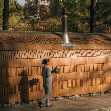 Iglu sauna exterior at Amankora's Paro Lodge with two figures standing before wooden structure surrounded by cypress trees.