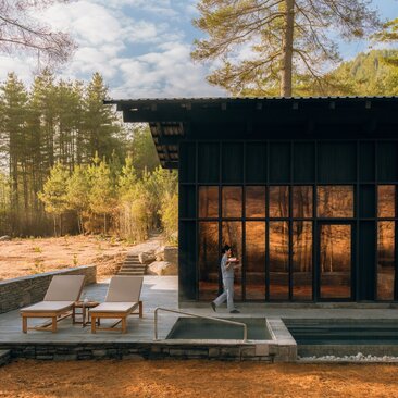 Spa house at Amankora's Paro Lodge with illuminated interior, wooden deck and forest setting at dusk.