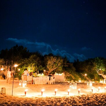 Beach dinner setup at Amanyara with candlelit tables on sand at dusk, Turks and Caicos.