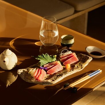 Akari dining venue at Amanzoe resort, plated dish with sashimi and garnishes under warm lighting.