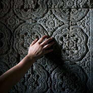 Hand tracing ornate stone carving at Prambanan Temple, Amanjiwo.