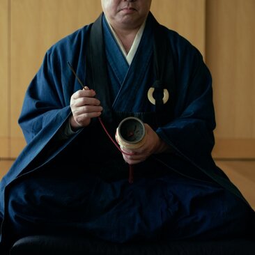Monk in blue robes holding meditation beads at Aman Tokyo, Japan.
