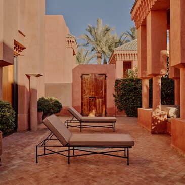 Pavilion terracotta courtyard at Amanjena resort in Morocco, with bench seating and potted plants.