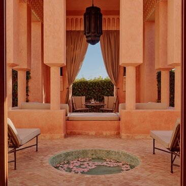 Pavilion interior at Amanjena resort, Morocco, with symmetrical archways in terracotta tones and views of gardens beyond.