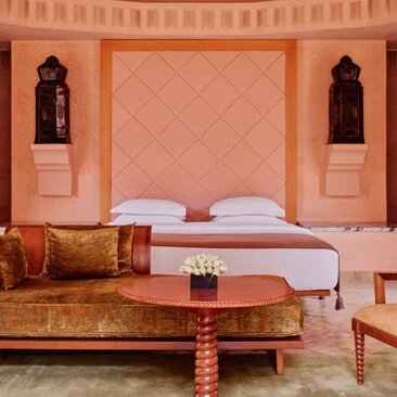 Pavilion bedroom at Amanjena resort in Morocco, featuring terracotta walls, arched alcoves, and a bed with decorative pillows.