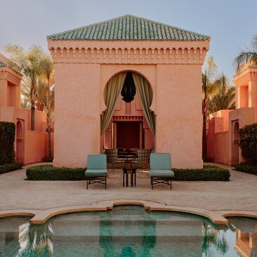 Amanjena pavilion courtyard with pink walls, arched doorway, and reflecting pool in Morocco.