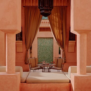 Villa interior with symmetrical terracotta archways, draped rust curtains, and central seating area at Amanjena resort, Morocco.