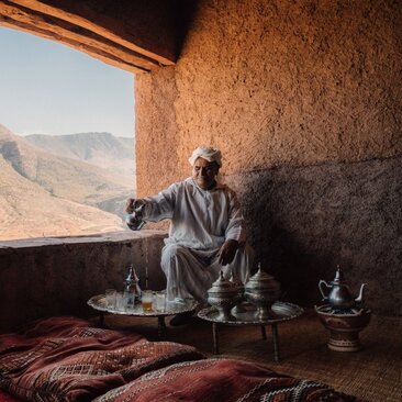 Berber family member seated at a low table inside a traditional riad at Amanjena, Morocco, with Atlas Mountains visible through the open doorway.