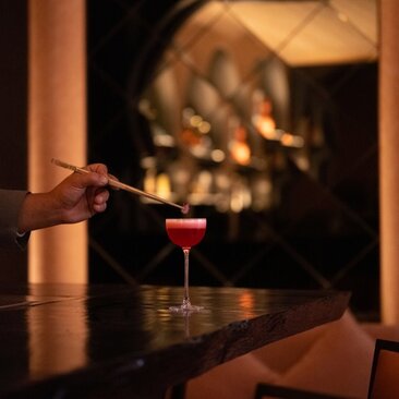Hand holding a cocktail at Arva Bar, Amanjena, Morocco, with lanterns glowing in the background.