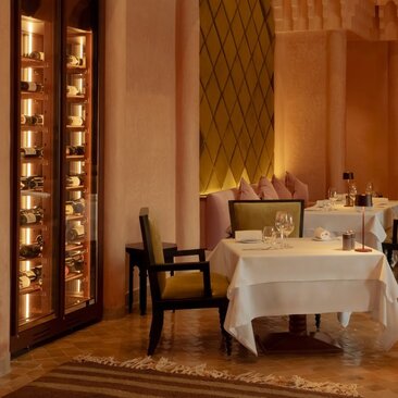Amanjena dining venue with warm lighting, white-dressed table, and illuminated wine display.