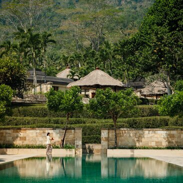 Amanjiwo's stone pool pavilions overlook emerald waters with forested hillside beyond.