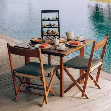 Bhutanese-inspired high tea setting at Amankora with wooden table, chairs, and tiered pastry stand overlooking water in Punakha.