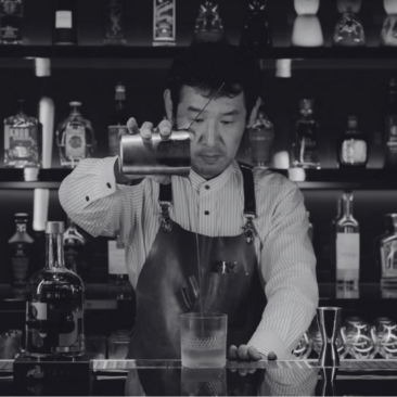 Mixologist Kawasaki crafting a cocktail at Amanoi's bar, black and white photograph.