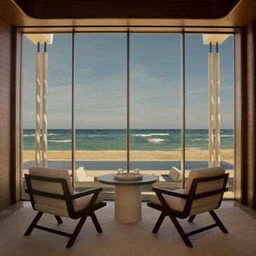 Two mid-century chairs face expansive ocean views through floor-to-ceiling windows at Amanvari beachfront casita.