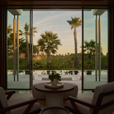 Interior view of Estuary Casita at Amanvari, Mexico, showing open glass doors framing palm trees and estuary landscape at dusk.