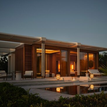 Estuary Casita at Amanvari with illuminated interiors reflected in still water at dusk, Mexico.