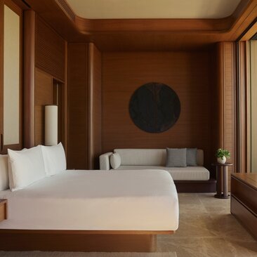 Principal bedroom with warm timber finishes, bed with white linens, and circular artwork at Amanvari, Mexico.