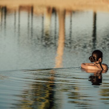Guest swimming in still water at Amanvari, Mexico, with wooden posts reflected in the surface.