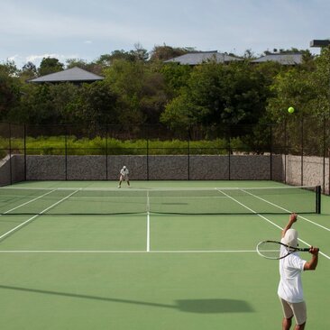 Tennis court at Amanoi with player preparing to serve, surrounded by verdant Vietnamese landscape.