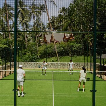 Padel court at Amanpuri, Thailand, with players in action on the grass court surrounded by tropical vegetation.