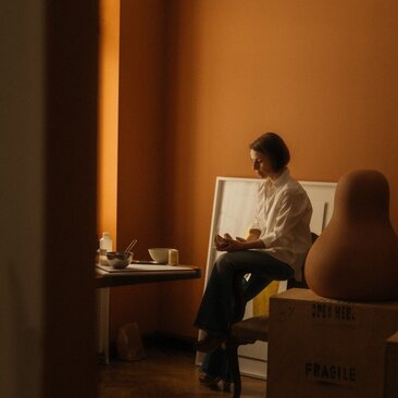 Studio portrait of Nikomachi Karakostanoglou at Amanzoe, Greece, seated beside a mirror in warm golden light.