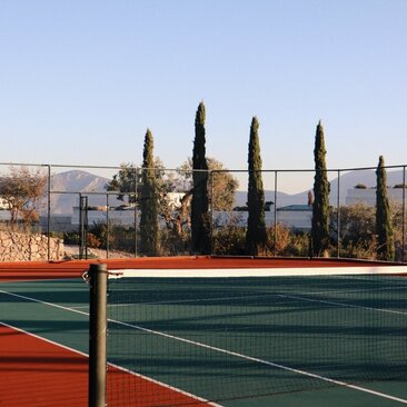 Tennis court at Amanzoe with Aegean Sea views and cypress trees, Greece.