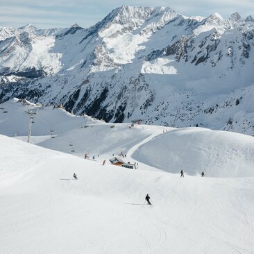 Skieurs sur les pistes enneigées d'Aman Le Mélézin, avec montagnes enneigées en arrière-plan.