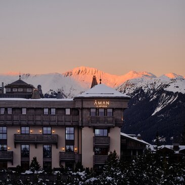 Aman Le Mélézin resort exterior at dusk, snow-covered peaks glowing in alpine twilight.