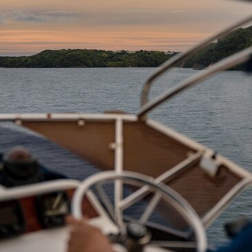 Sunset cruise from Amanemu resort's boat, steering wheel in foreground with calm waters and coastline at dusk.