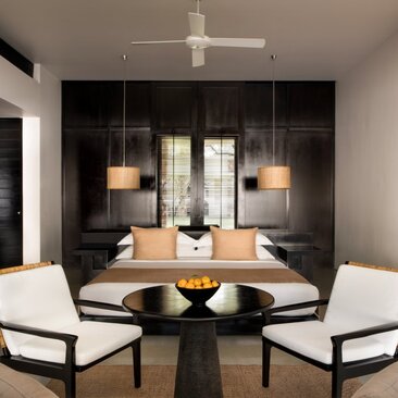 Amansara suite interior with dining table, contemporary chairs, and pendant lighting beneath dark feature wall.