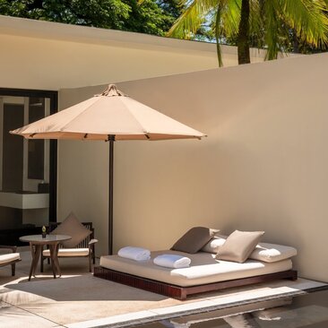 Amansara pool suite exterior with shaded daybed and umbrella against cream wall.