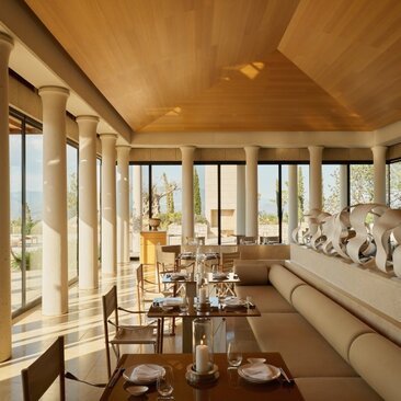 Akari dining venue at Amanzoe with wooden interiors, floor-to-ceiling windows overlooking the Aegean Sea, and intimate table settings.