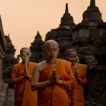 Buddhist monks in saffron robes at Amanjiwo at dawn, with temple silhouettes behind.