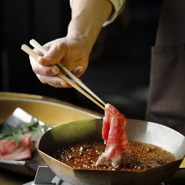 アマン京都のすきやき料理で、箸を使って牛肉を鍋に入れる様子。