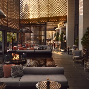 Aman New York's garden terrace lounge at dusk, with fireplace, seating areas, and latticed screens creating intimate corners.