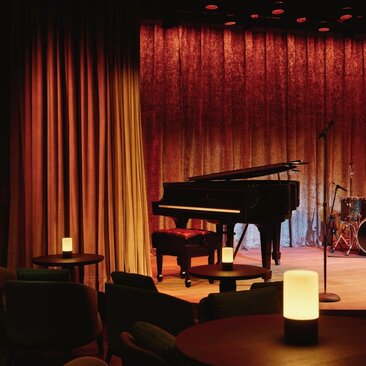 Interior do The Jazz Club no Aman New York, com palco iluminado em vermelho e cortinas douradas.