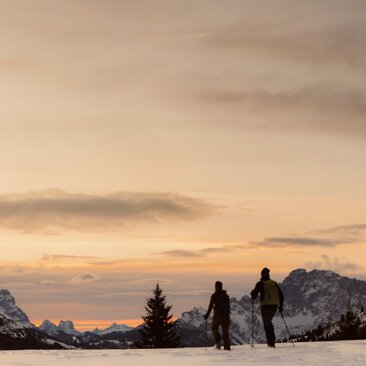 Skiers at Aman Rosa Alpina pause on snowy slopes at dusk, Italian Alps beyond.
