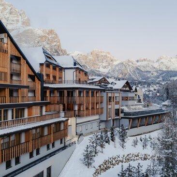Aman Rosa Alpina exterior with snow-covered Alpine peaks and forested valley in winter.