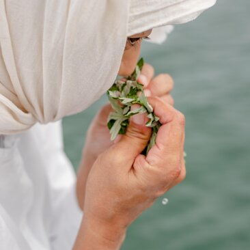 Hand holding fresh herbs against turquoise water at Amanemu resort, Japan.