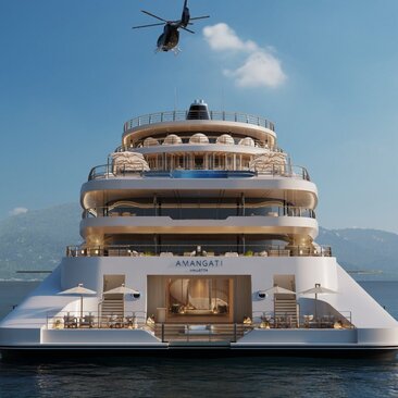 Aerial view of a superyacht moored at Amanyara, with a helicopter overhead and mountain backdrop.