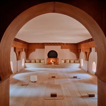 Amanjena's yoga studio with wooden archway, spa beds and serene lighting.