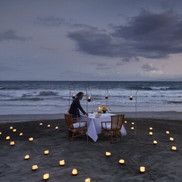 Dîner en bord de mer au coucher du soleil à Amankila, avec bougies illuminant le sable de la plage.