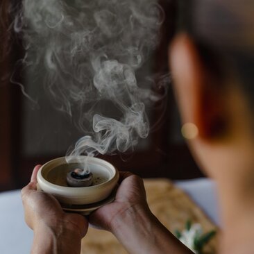 Hands holding a ceramic bowl with aromatic smoke rising from it during a wellness ceremony at Amanpulo.