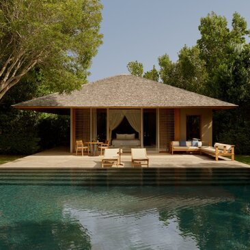 Alcove pool pavilion at Amanyara resort with thatched roof and wooden seating beside turquoise water.