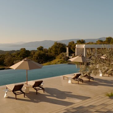 Villa pool overlooking the Aegean Sea at Amanzoe, Greece, with loungers on the terrace at sunset.