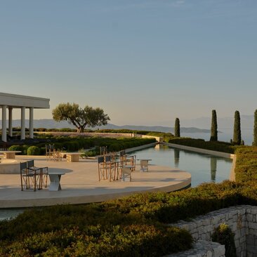 Firepit seating area overlooking reflecting pools at Amanzoe, Greece, at dusk.