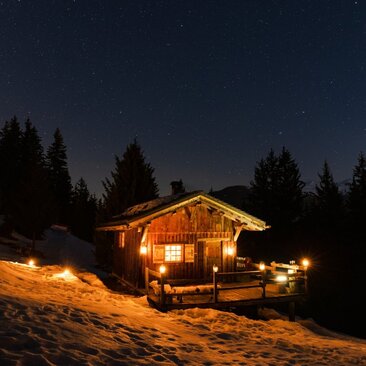 Wooden chalet glowing warmly at dusk in the French Alps, surrounded by evergreen trees and snow at Aman Le Mélézin.