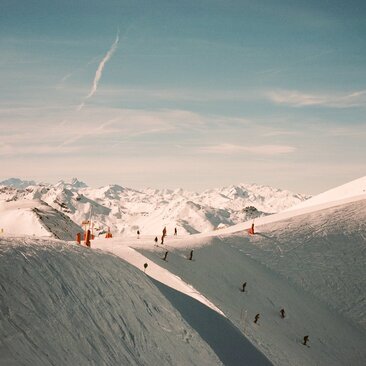 Skiers descend snowy slopes at Aman Le Mélézin in the French Alps, beneath clear skies.