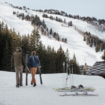 Ski valet at Aman Le Mélézin prepares equipment on snow-covered slope with Alpine forest backdrop.