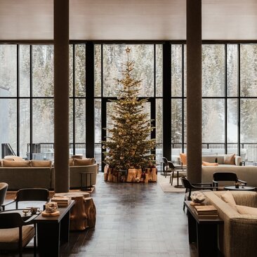 Festive dining room at Aman Rosa Alpina with decorated Christmas tree framed by large windows overlooking Alpine landscape.